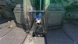 John-117 driving an M12 Chaingun Warthog into the entrance of the Cartographer facility while under attack by Covenant forces. From Halo: Combat Evolved Anniversary campaign level The Silent Cartographer.